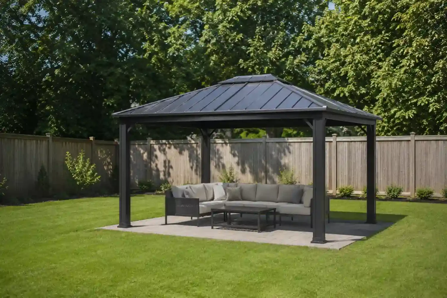 Well built hardtop gazebo with dark aluminum frame and neutral sectional seating on a paver patio in a clean open backyard with wood privacy fence.
