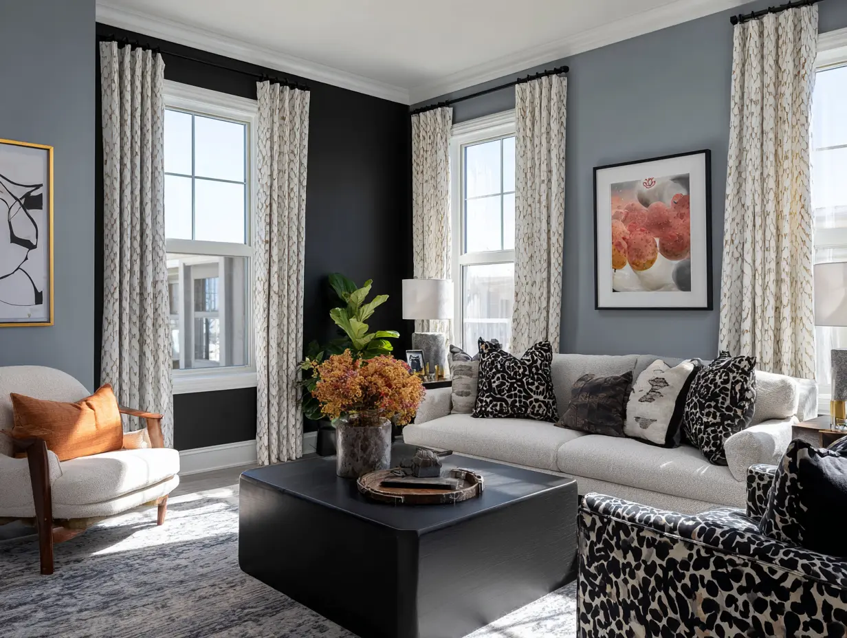 Home staging tips for living room: gray neutral sofa with mixed-pattern pillows, modern black accent wall, floor-to-ceiling curtains, statement coffee table with fresh flowers and warm table lamp.