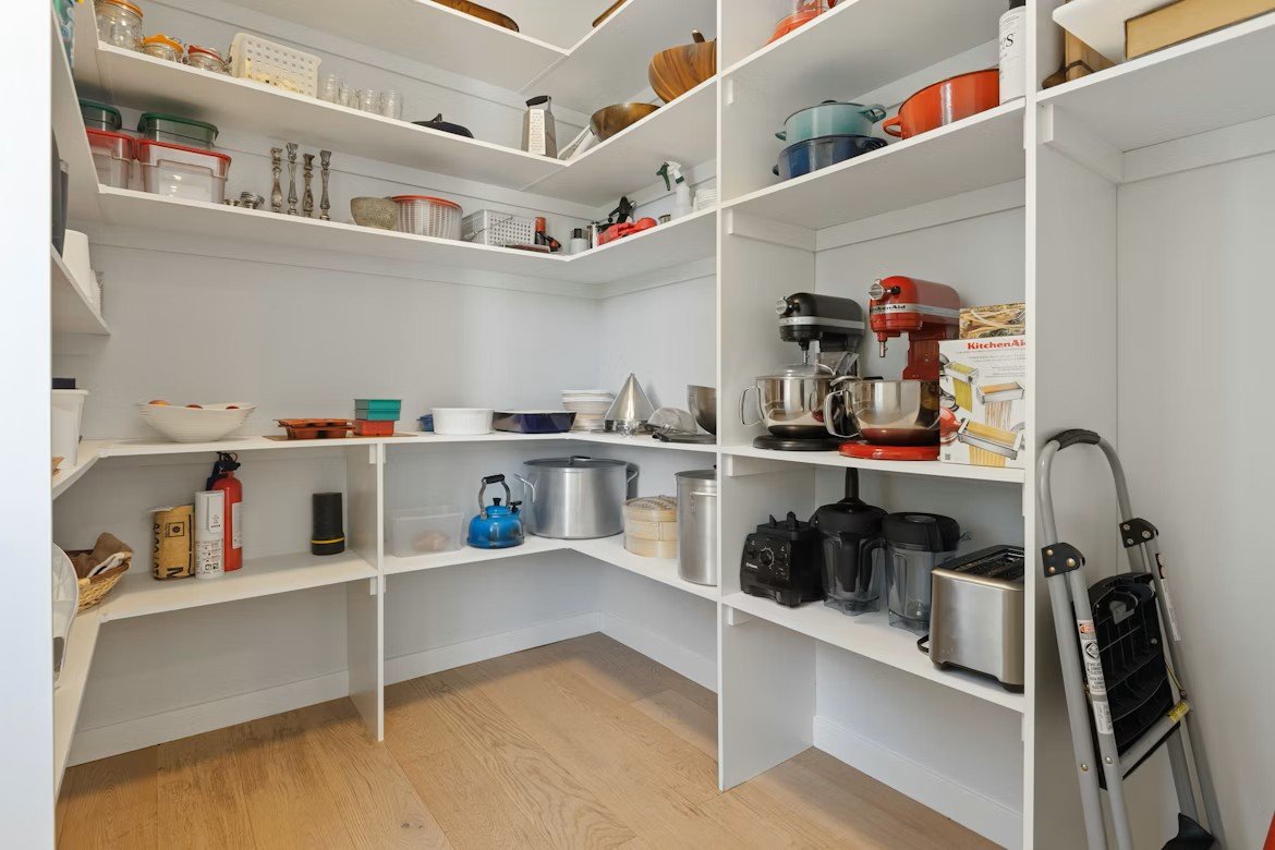 Well organized walk-in pantry with white shelving, kitchen appliances, cookware, and storage containers.