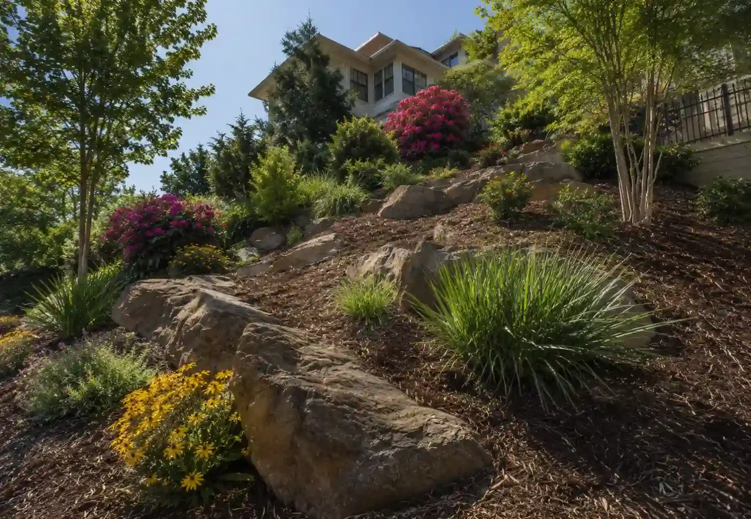 Terraced hillside landscaping with large boulders and blooming perennial plants for seasonal slope maintenance