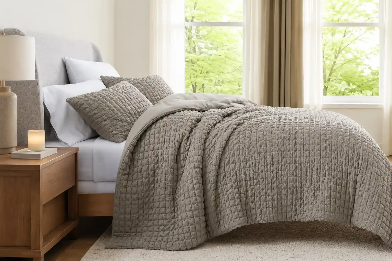 Earthy tones bedroom featuring mushroom gray quilted bedding, crisp white pillows, a warm wood nightstand, soft natural light, and warm minimalist bedroom styling with layered neutral textures.