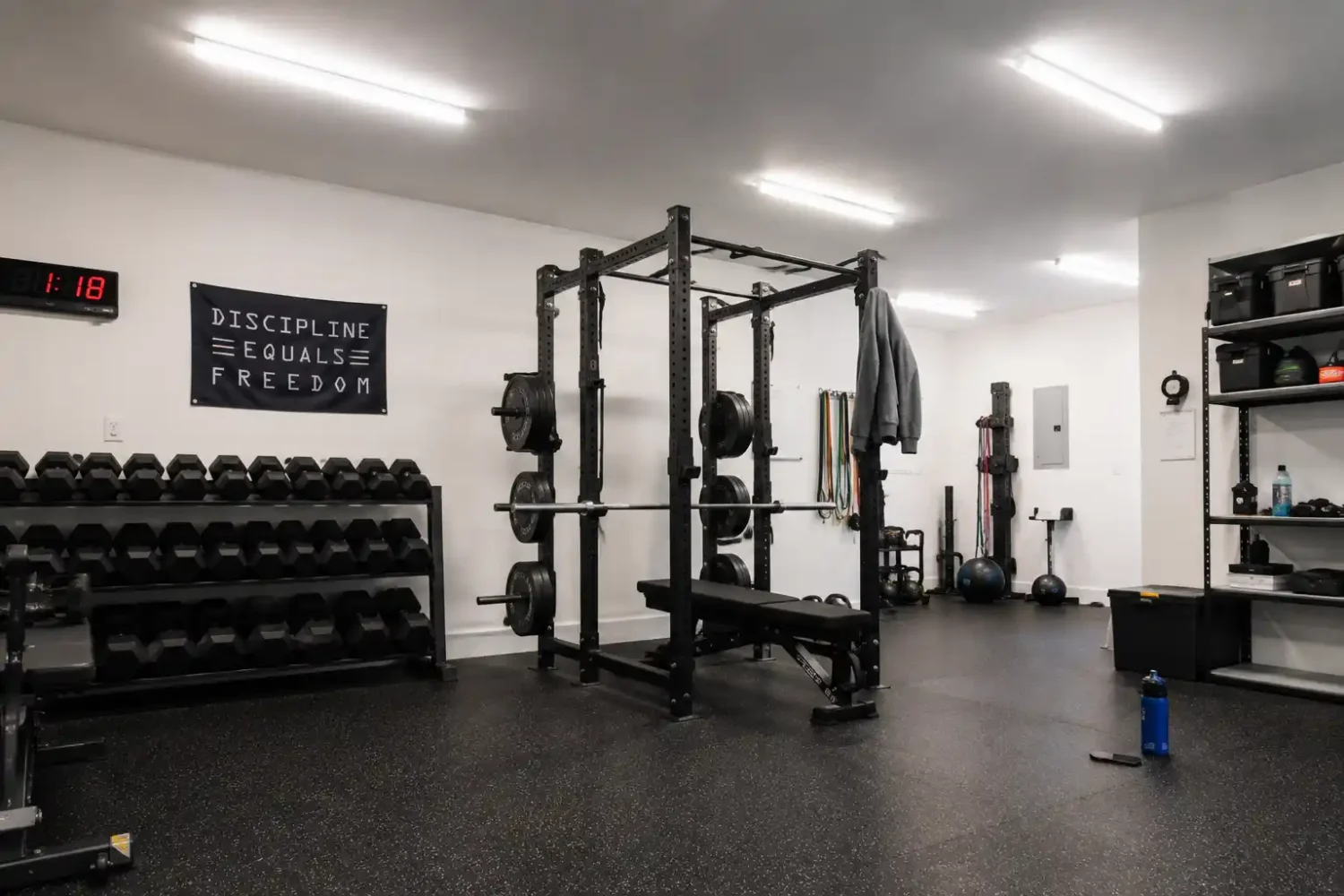 Garage gym lighting installed across a home gym with rack, dumbbells, and storage area.