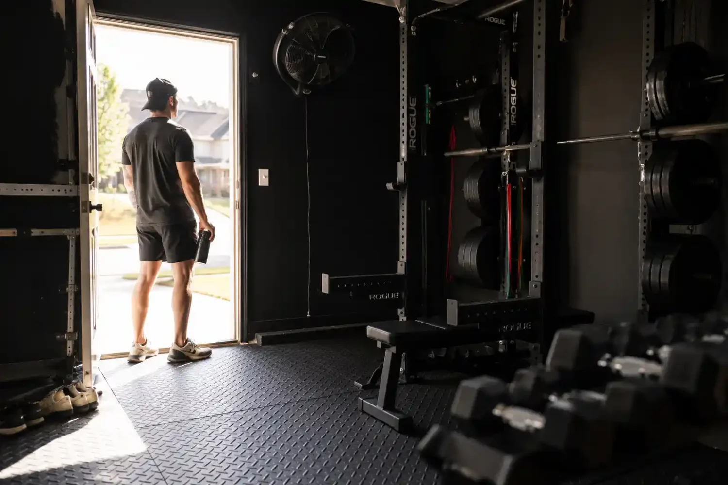 Man standing in garage gym doorway with wall mounted fan power rack and rubber flooring ready to train.