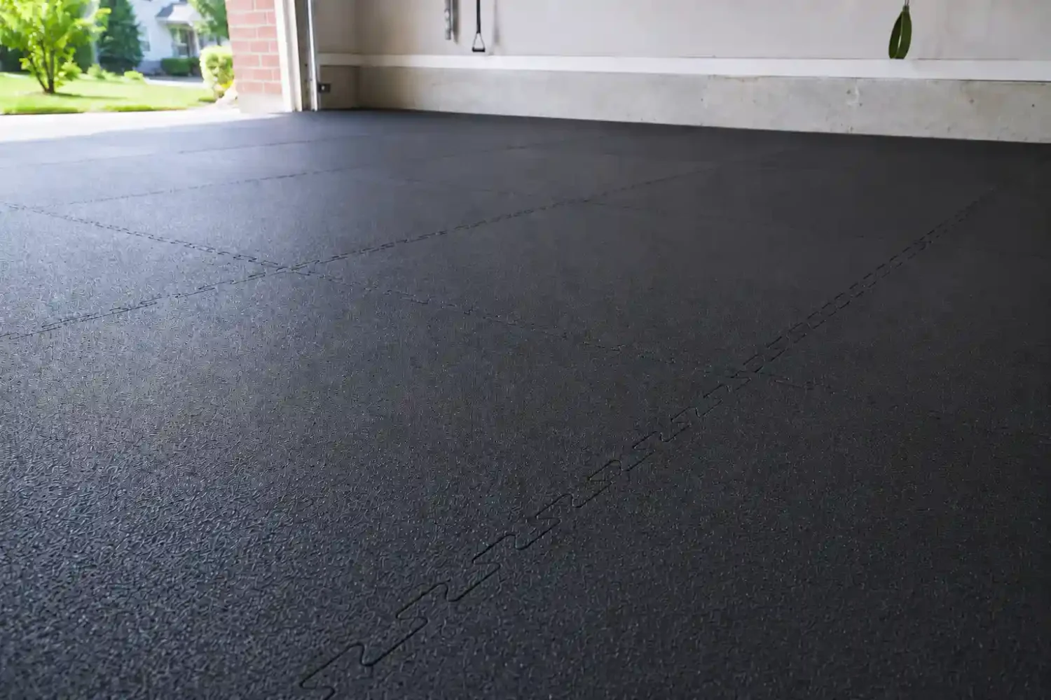 Dark interlocking rubber gym mats installed across a garage floor with visible puzzle seams and natural light from an open garage door.