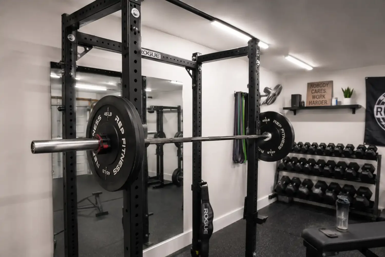 Squat rack with overhead lighting positioned forward of the bar, mirror reflecting an evenly lit lifting area.